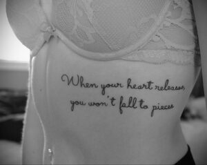 Фото тату на боку с надписью "When your heart releases, you won't fall to pieces". Черно-белый рисунок татуировки с красивым шрифтом.