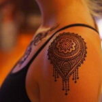 Фото татуировки на плече, выполненной в стиле хенд-поук (hand-poke), с изображением сложного геометрического узора в коричневых тонах.