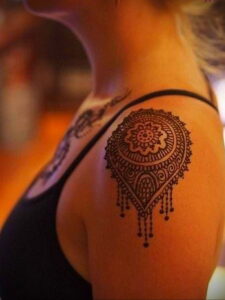 Фото татуировки на плече, выполненной в стиле хенд-поук (hand-poke), с изображением сложного геометрического узора в коричневых тонах.