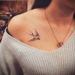 Фото тату: Небольшая татуировка ласточки в полете, выполненная в технике blackwork, на женском плече. Изящный рисунок татуировки.
