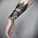 Черно-белая татуировка леса на предплечье, с геометрическим узором внизу. Детализированный рисунок деревьев и текстура коры.