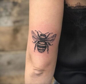 Фото минималистичной татуировки пчелы на локте, выполненной в технике blackwork с использованием тонких линий и четких контуров.
