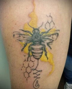 Фото тату с изображением шмеля на фоне сот. Татуировка выполнена в черно-серых тонах с использованием желтых акцентов для имитации меда.
