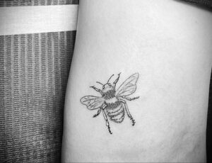 Маленькая татуировка пчелы, выполненная в технике blackwork. Изображение состоит из четких черных линий и точек, создающих силуэт насекомого.