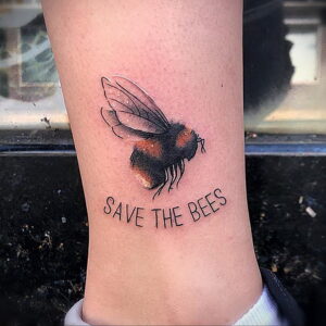 Миниатюрная татуировка шмеля и надписи 'Save the Bees' на лодыжке. Яркие цвета, реалистичный рисунок, призыв к защите пчел.