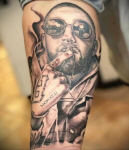 Фотография реалистичной татуировки на руке с изображением Mac Miller в солнцезащитных очках, держащего сигарету.