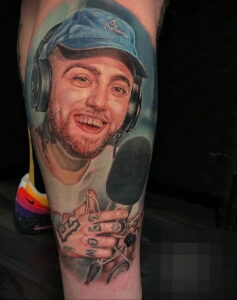 Цветное фото тату на предплечье с изображением Mac Miller в кепке, с наушниками и микрофоном, символизирующим его музыкальную карьеру.