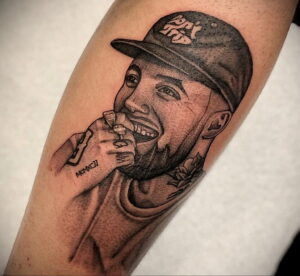 Черно-белое фото тату на предплечье с изображением Mac Miller в кепке, с сигаретой в руке и цветком рядом.