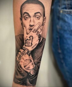 Черно-белое фото тату на предплечье с реалистичным портретом Mac Miller, с татуировками на пальцах, кольцами и логотипом Pittsburgh Pirates.