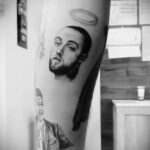 Черно-белое фото тату на руке с изображением Mac Miller с нимбом над головой, символизирующим его уход. Внизу виден фрагмент его портрета.