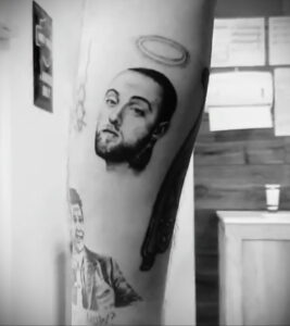 Черно-белое фото тату на руке с изображением Mac Miller с нимбом над головой, символизирующим его уход. Внизу виден фрагмент его портрета.