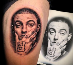 Черно-белое фото тату на предплечье с реалистичным портретом рэпера Mac Miller, с детально проработанными татуировками на пальцах и кольцами.
