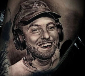 Фото тату на руке с реалистичным портретом Mac Miller в кепке и наушниках. Детализированный рисунок татуировки.