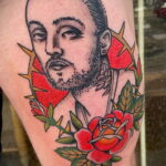 Фото тату на руке с реалистичным портретом Mac Miller, окруженного красной колючей проволокой и красными розами. Детализированный рисунок татуировки.