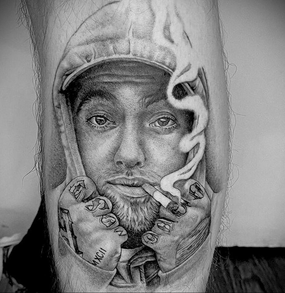 Черно-серая реалистичная татуировка Mac Miller с сигаретой во рту и кепкой на голове на руке.