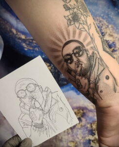 Цветная татуировка Mac Miller в скафандре космонавта на руке, с эскизом рядом и элементами цветочного фона.