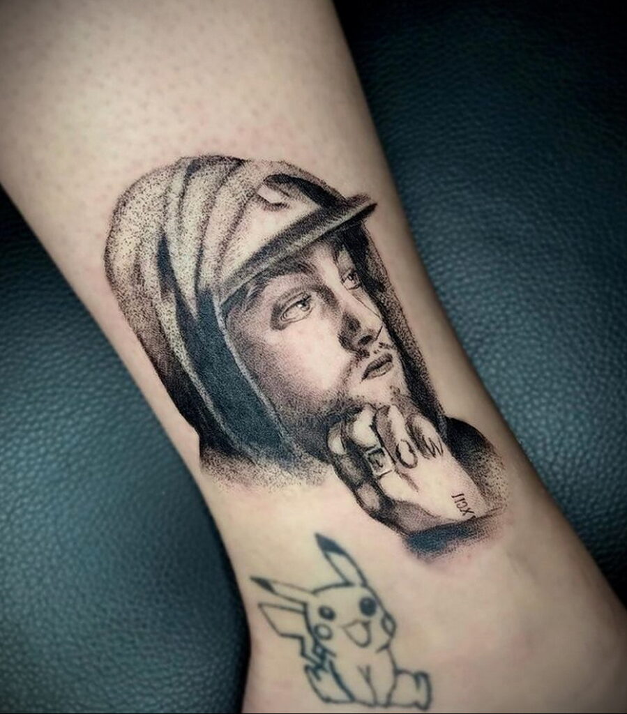 Черно-серая реалистичная татуировка Mac Miller в кепке на руке, с добавлением небольшого рисунка Пикачу.
