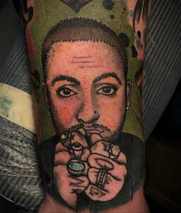 Цветная татуировка портрета Mac Miller на руке, выполненная в стиле поп-арт с использованием ярких цветов и контрастных линий.