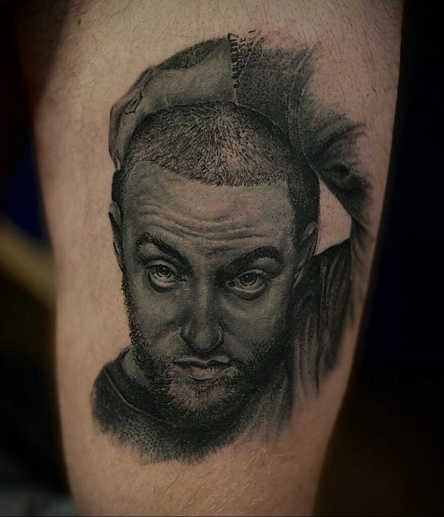 Черно-серая реалистичная татуировка портрета Mac Miller на предплечье. Детализированное изображение лица и кепки.