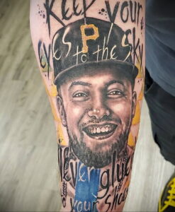 Фото тату на руке с ярким портретом Mac Miller, улыбающегося и смотрящего в камеру. Рисунок татуировки с использованием ярких цветов и надписей.