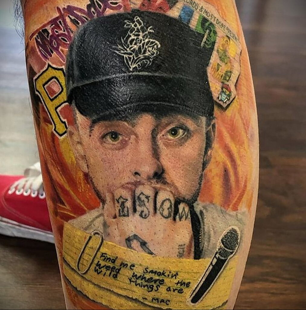 Фото тату на руке с ярким портретом Mac Miller на фоне огня. Детализированный рисунок татуировки с использованием ярких цветов.