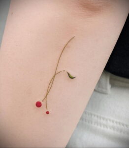 Фото минималистичной татуировки двух красных вишен с зеленым листом, выполненной тонкими линиями. Нежный и изящный рисунок татуировки.