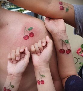 Фотография парных татуировок с изображением двух красных вишен на руках разных людей. Символ любви, дружбы и единства.