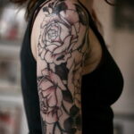 Фото татуировки на плече с изображением черных роз. Стиль blackwork, характеризующийся использованием только черного цвета и графичных линий.