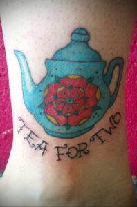 Фото татуировки чайника с розой внутри и надписью 'Tea for Two' на лодыжке.