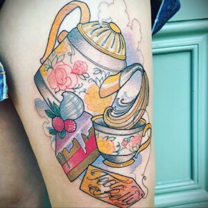 Фото тату: красочный рисунок чайника, чашки, пирожных и надписи 'Teacups & Jelly' на бедре. Татуировка выполнена в акварельном стиле.