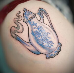 Татуировка на руке с изображением чайника, украшенного голубыми цветами. Нежный и изящный рисунок татуировки.