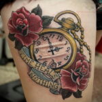 Фото тату на бедре с изображением красных роз, карманных часов и надписи "Time heals nothing". Детализированный рисунок татуировки.