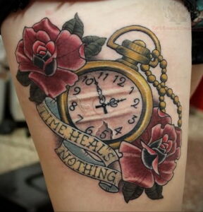 Фото тату на бедре с изображением красных роз, карманных часов и надписи "Time heals nothing". Детализированный рисунок татуировки.