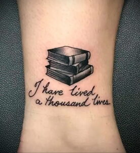 Фото тату на запястье с изображением небольшой стопки книг и надписью 'I have lived a thousand lives'. Простой и элегантный рисунок татуировки.