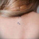 Фото минималистичной татуировки знака зодиака Стрелец, выполненной тонкими линиями на коже у основания шеи. Небольшой рисунок татуировки.