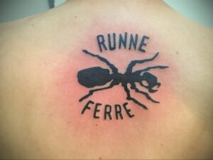 Фото тату муравья на спине, окруженного надписью "Runne Ferre". Черно-белый рисунок.