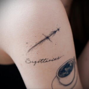 Фото татуировки на плече с изображением падающей звезды и надписи "Sagittarius". Изящный и минималистичный рисунок.