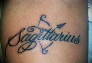 Фото тату: надпись "Sagittarius" с маленькой стрелой, татуировка на руке, шрифт, знак зодиака.
