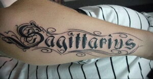 Фото тату на руке с надписью 'Sagittarius' выполненной в каллиграфическом стиле. Элегантный и стильный рисунок татуировки.