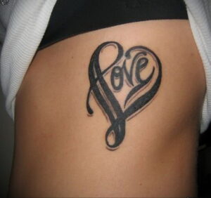 Фото тату: надпись "Love", стилизованная под форму сердца, на боку. Черно-белая татуировка, выполненная в каллиграфическом стиле. Элегантный рисунок татуировки.