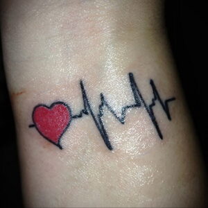 Фото татуировки на запястье в виде красного сердца, соединенного с линией пульса. Символ жизненной силы и любви.