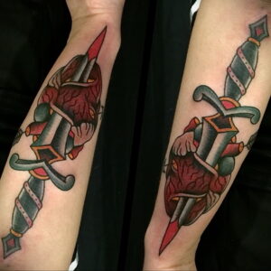 Фото татуировки на предплечьях: два сердца, пронзенных кинжалами, с лентами и узорами. Симметричный рисунок в стиле олд скул.