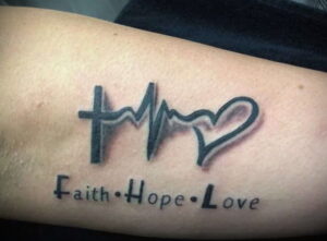 Фото татуировки на предплечье: крест, пульс в форме сердца и надпись 'Faith, Hope, Love'. Символическая татуировка, отражающая основные христианские добродетели.