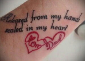 Фото тату на запястье: надпись 'Released from my hands sealed in my heart' и два сердца с надписями 'Mom' и 'Dad'. Трогательный рисунок татуировки в память о родителях.