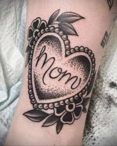 Фото тату на предплечье: сердце, выполненное в технике dotwork, с надписью 'Mom' внутри. Черно-белое изображение, детализированная проработка.