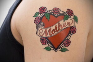 Фото татуировки на плече: красное сердце с надписью 'Mother', окруженное розами. Классический стиль и яркие цвета.
