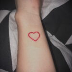 Фото тату маленького красного сердца на запястье, выполненного тонкой линией. Минималистичный дизайн, символизирующий любовь и страсть.