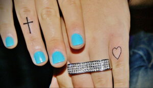 Фото тату с изображением креста и сердца на пальцах. Черно-белые рисунки, минималистичный стиль, небольшие татуировки, символическое значение.