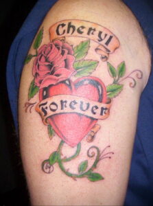 Фото тату на плече: изображение розы, сердца и надписи 'Cheryl Forever' на ленте, выполненное в ярких цветах.