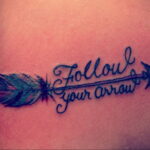 Фото тату: стрела с яркими перьями и надписью 'Follow your arrow'. Красивый рисунок татуировки для девушек, выполненный в цветном стиле.